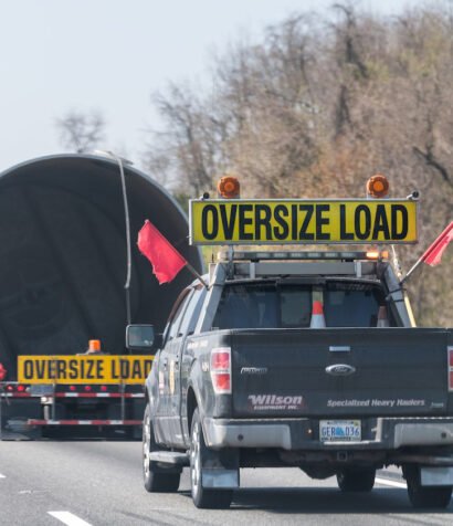 Woodstock, USA - April 18, 2018: Hauler truck trailer vehicle hauling oversize load of concrete pipe tube on interstate highway road in Virginia with yellow warning signs and red flags